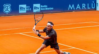 Tennista in azione su campo da tennis in terra rossa.