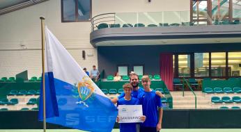 Tre atleti di San Marino in posa con la bandiera e un cartello.