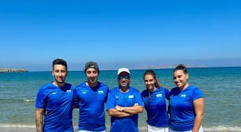 Cinque persone in divise blu e bianche sulla spiaggia.