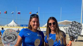 Due giocatrici di beach tennis con trofei e racchette sulla spiaggia.