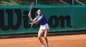 Tennista in azione su campo in terra rossa, sfondo con logo Wilson.